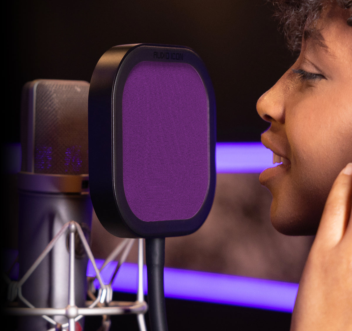 Person in a recording studio with a microphone and pop filter.