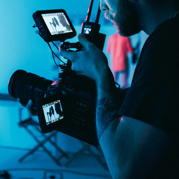 Person holding a video camera with a monitor displaying footage, with a blue tint.