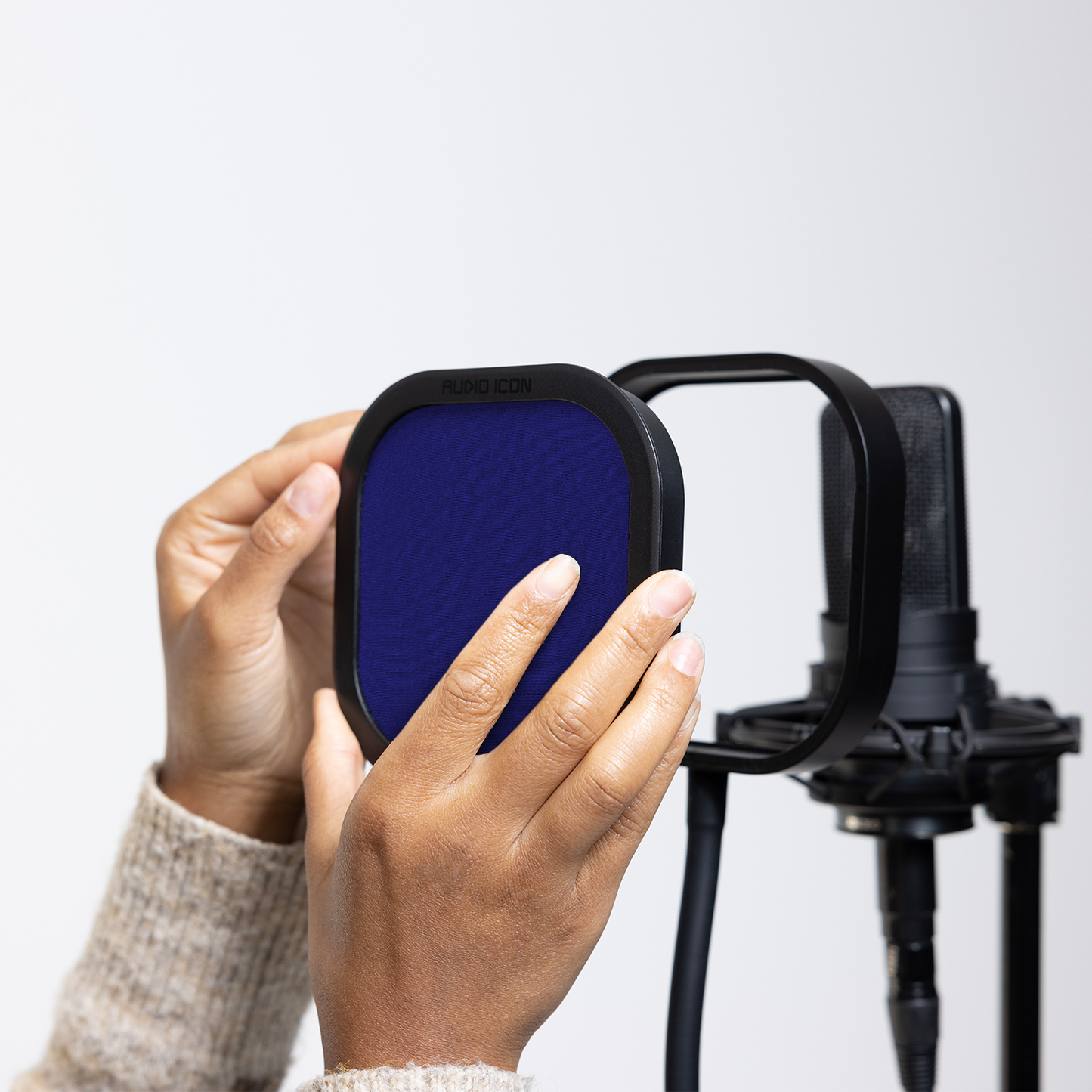 Hands installing the blue Audio Icon Flex Pro removable acoustic enclosure on a studio microphone for vocal recording, podcasting, streaming, and voice-over.