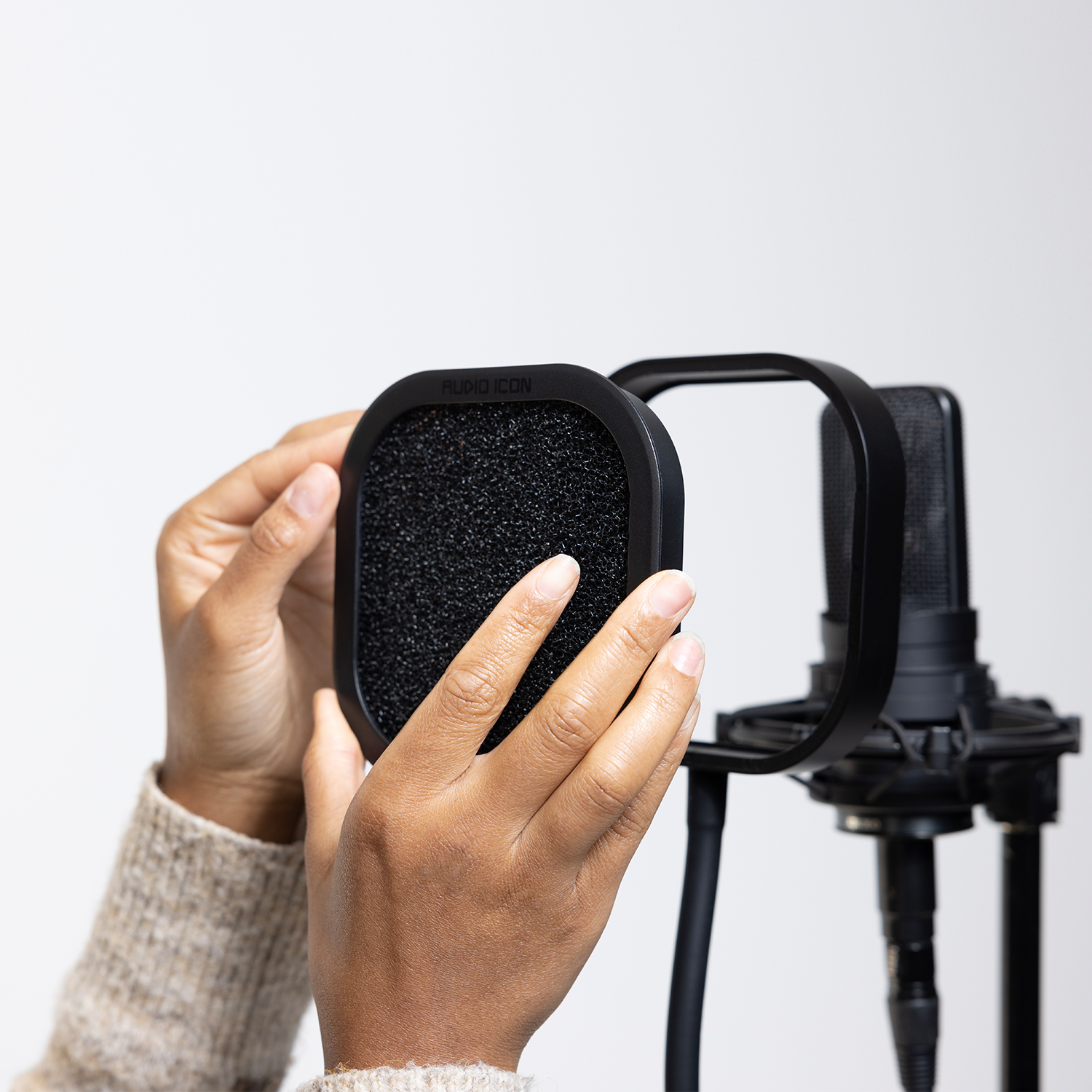 Hands installing the foam Audio Icon Flex Pro removable acoustic enclosure on a studio microphone for vocal recording, podcasting, streaming, and voice-over.