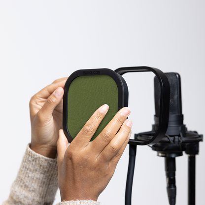 Hands installing the green Audio Icon Flex Pro removable acoustic enclosure on a studio microphone for vocal recording, podcasting, streaming, and voice-over.