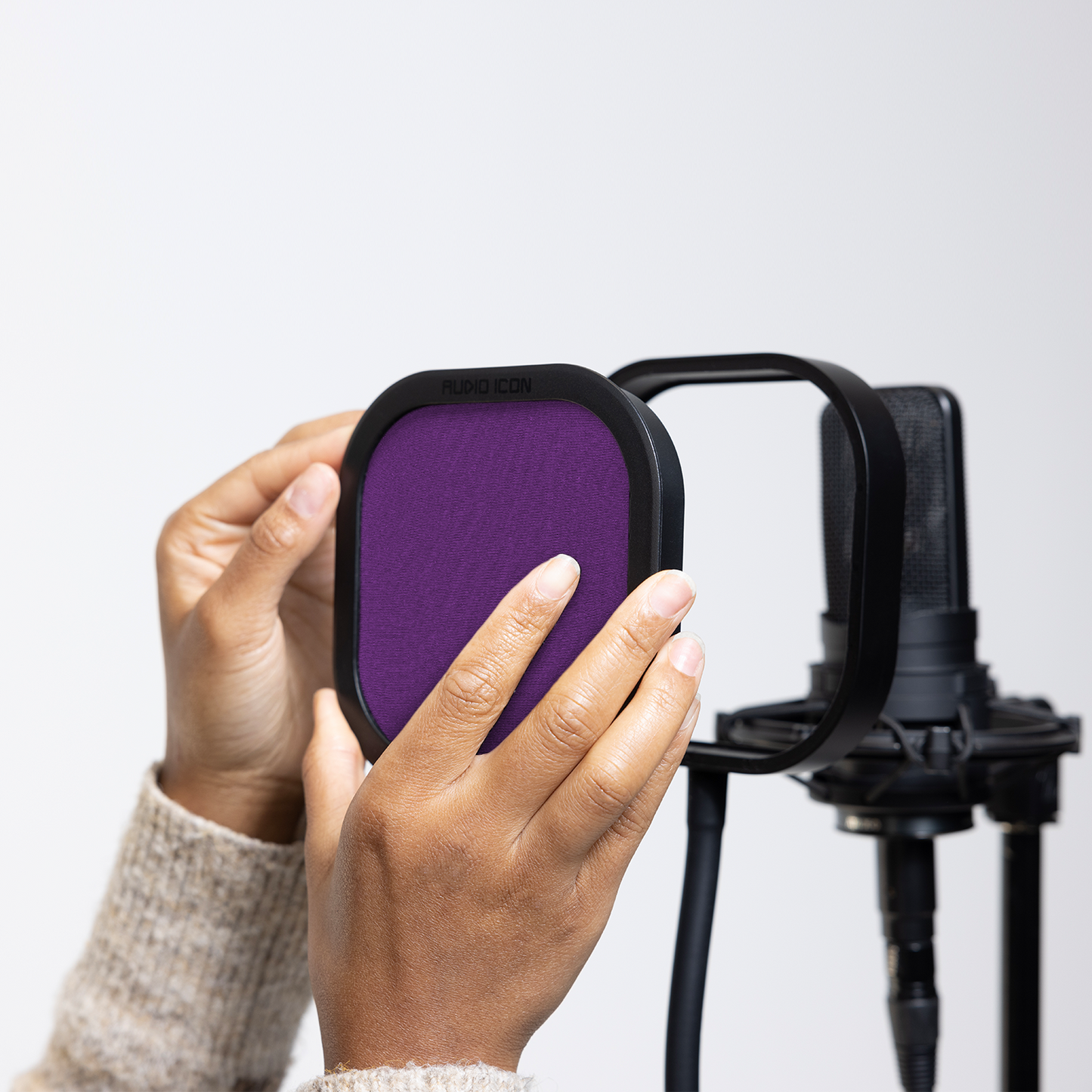 Hands installing the purple Audio Icon Flex Pro removable acoustic enclosure on a studio microphone for vocal recording, podcasting, streaming, and voice-over.