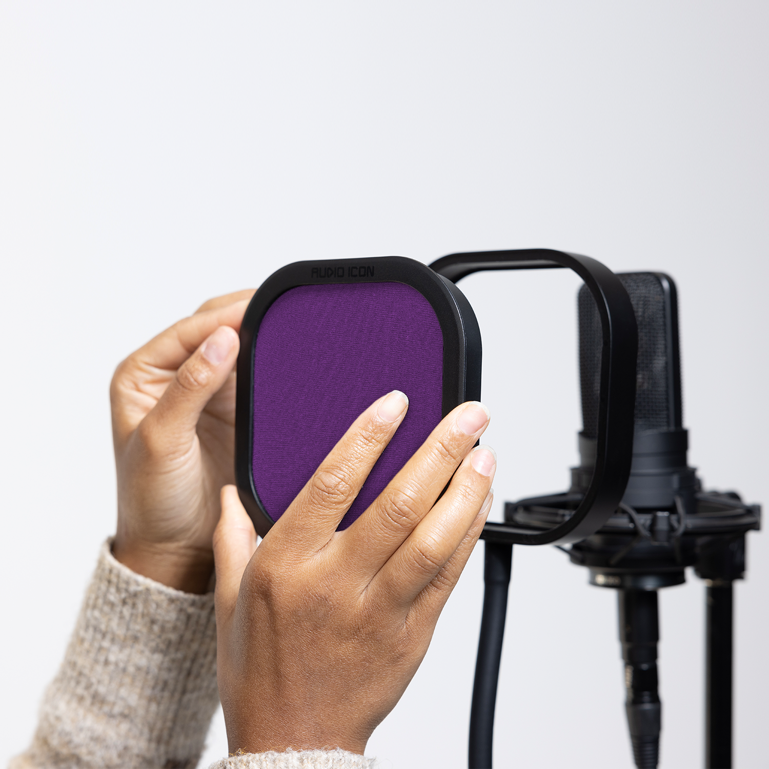 Hands installing the purple Audio Icon Flex Pro removable acoustic enclosure on a studio microphone for vocal recording, podcasting, streaming, and voice-over.
