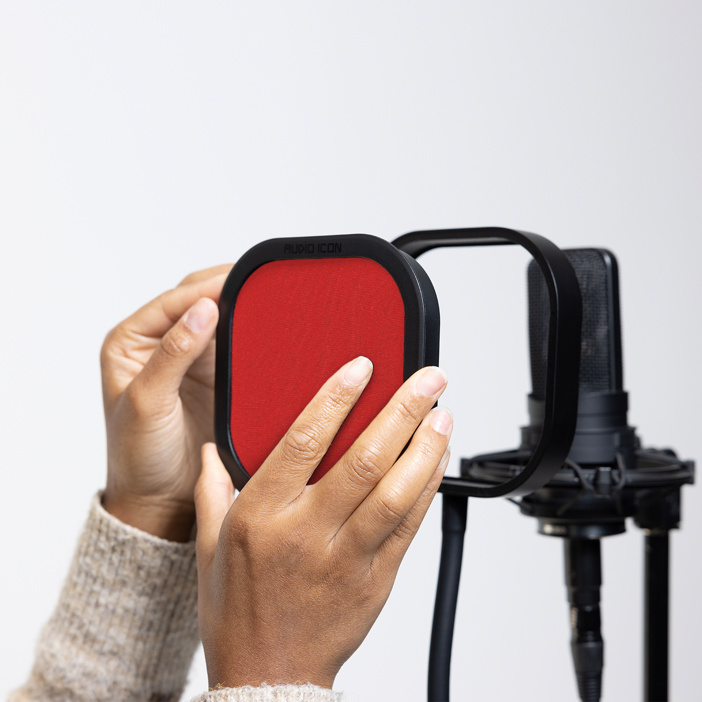 Hands installing the red Audio Icon Flex Pro removable acoustic enclosure on a studio microphone for vocal recording, podcasting, streaming, and voice-over.