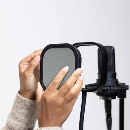 Hands installing the silver Audio Icon Flex Pro removable acoustic enclosure on a studio microphone for vocal recording, podcasting, streaming, and voice-over.