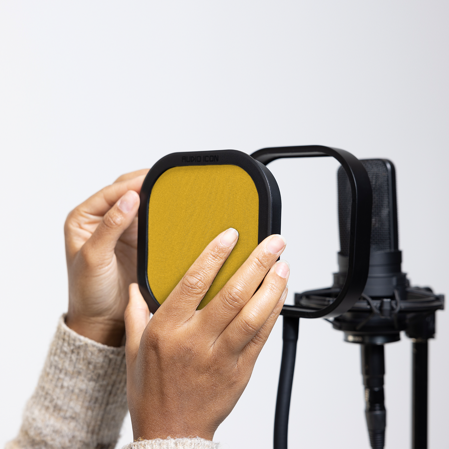 Hands installing the Yellow Audio Icon Flex Pro removable acoustic enclosure on a studio microphone for vocal recording, podcasting, streaming, and voice-over.