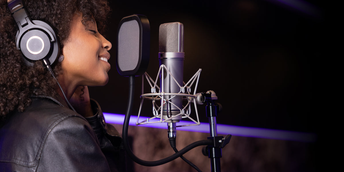 Woman singing into Flex Pro pop filter. Microphone and dark studio in background.