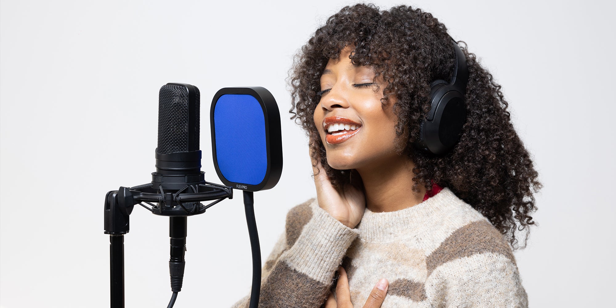 Woman with curly hair singing into a Flex Pro with blue mesh pop on microphone stand